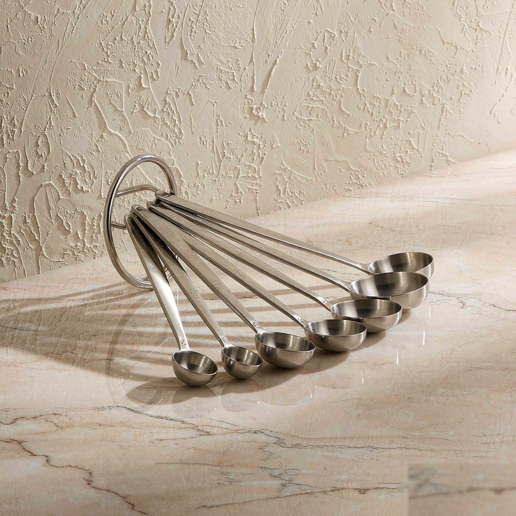 7-piece stainless steel magnetic measuring spoons fanned out on a marble countertop